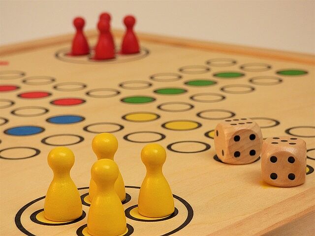 Ein Brettspiel mit roten und gelben Figuren. Zwei Würfel liegen ebenfalls auf dem Spielbrett.