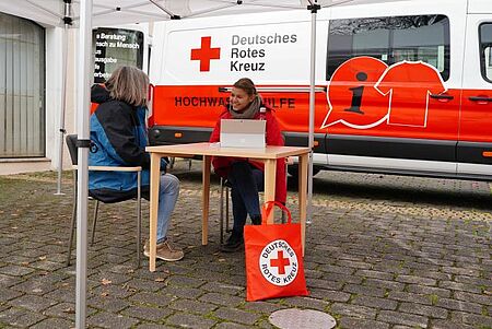 Symbolbild. Eine Frau vom DRK sitzt am Tisch und spricht mit einer anderen Frau