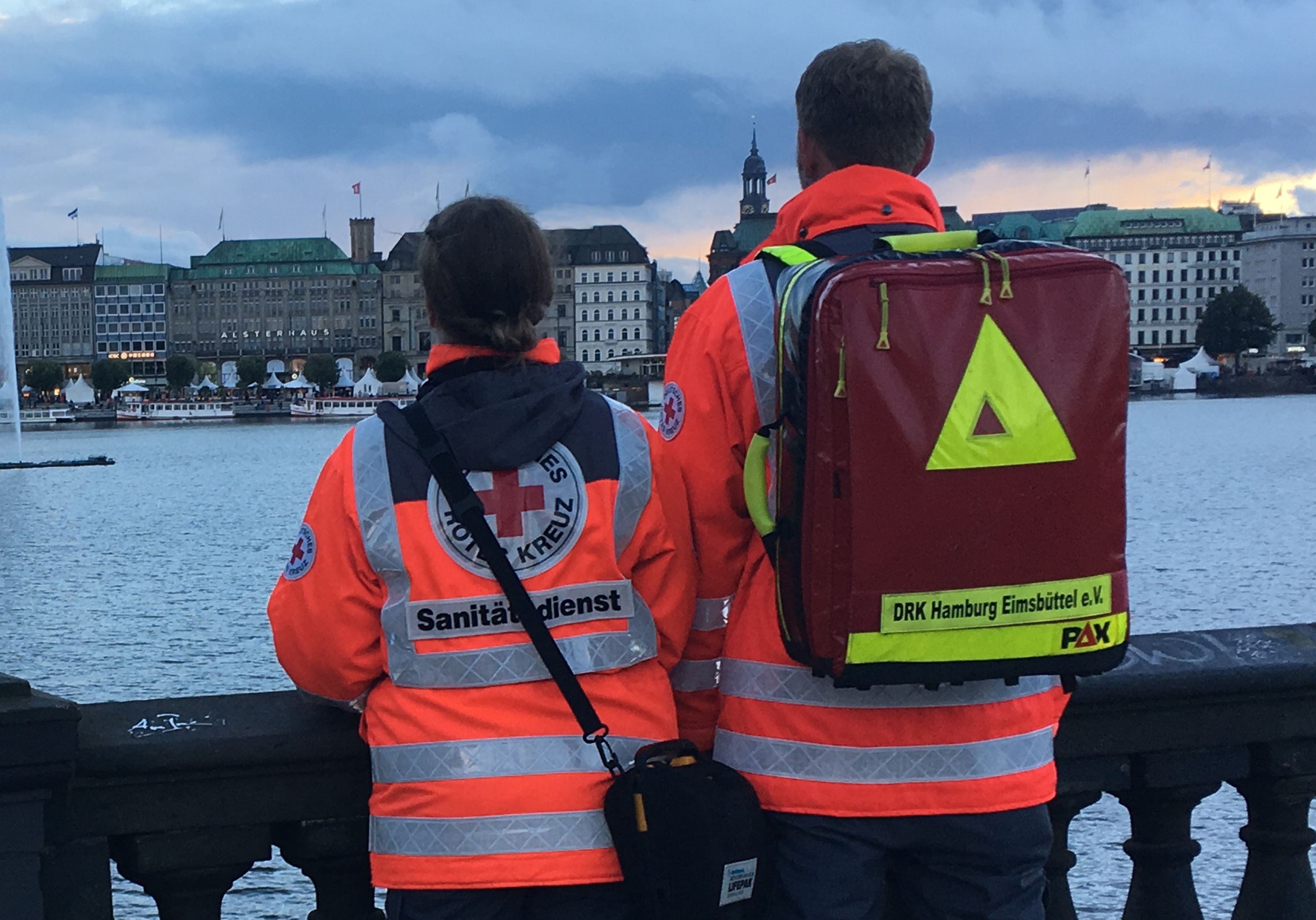 Zwei Sanitäter der Bereitschaft stehen auf der Kennedybrücke und blicken in Richtung Rathaus über die Alster