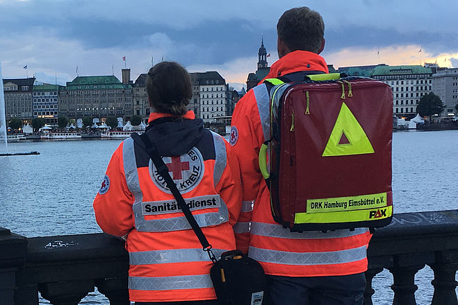 Zwei Sanitäter der Bereitschaft stehen auf der Kennedybrücke und blicken in Richtung Rathaus über die Alster