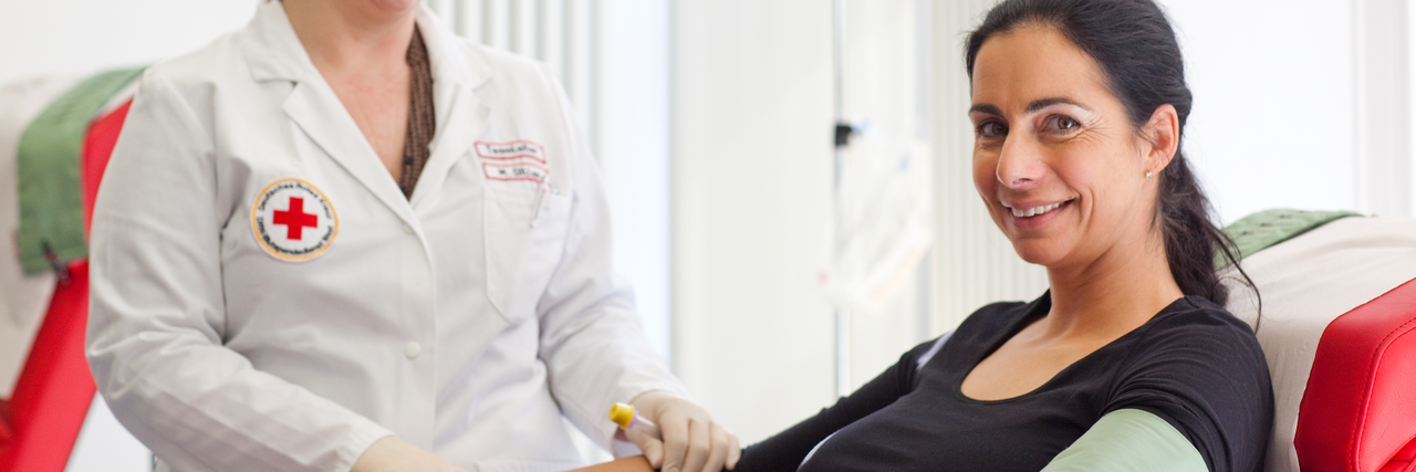 Eine Frag guckt freundlich in die Kamera und sitzt auf einem Stuhl, bereit für die Blutspende