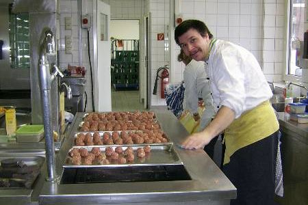 Ein Helfer steht in einer Großküche und bereitet Fleischbällchen zu.