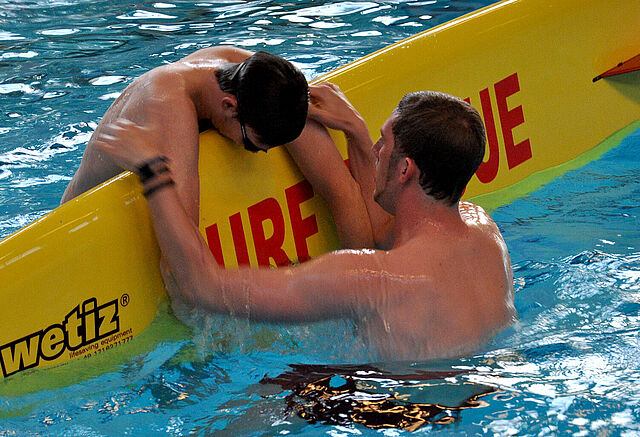 Ein Rettungsschwimmer in Ausbildung: Eine Person wird auf ein Rettungsbrett gerettet.