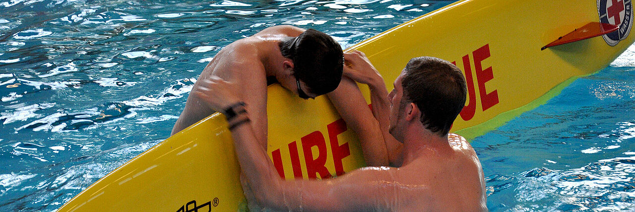 Ein Rettungsschwimmer in Ausbildung: Eine Person wird auf ein Rettungsbrett gerettet.