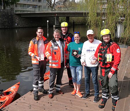 Einsatzkräfte, Menschen aus der Wasserwacht und Ehrenamtliche stehen zusammen mit der Fackel und Symbolen für die aktuellen Krisen 